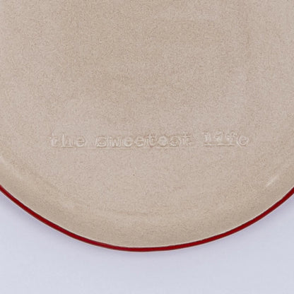 Prato raso em cerâmica com detalhe na borda vermelho e frase em baixo relevo "the sweetest life"